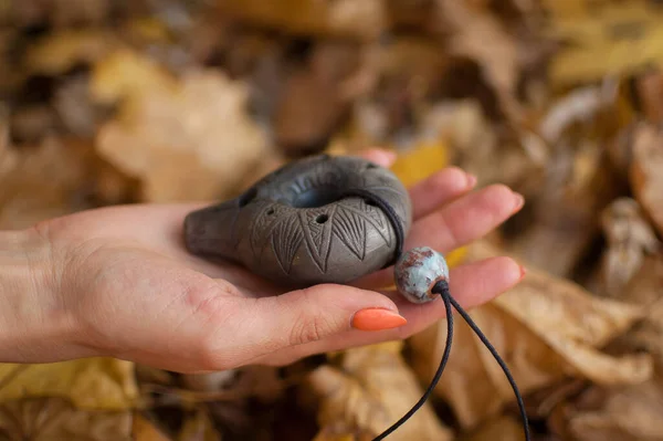 Female hand with orange manicure holds ceramic ocarina in the forest during autumn. Relaxing tranquil scene, traditional music concepts — Stock Photo, Image