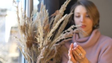 Genç bir kadın elinde gül kuvars taşından yapılmış bir yumurta gösteriyor. Kapalı alanda dikenli vazonun yanında duruyor. Kadın sağlığı konsepti, vumfit, imbuilding veya meditasyon