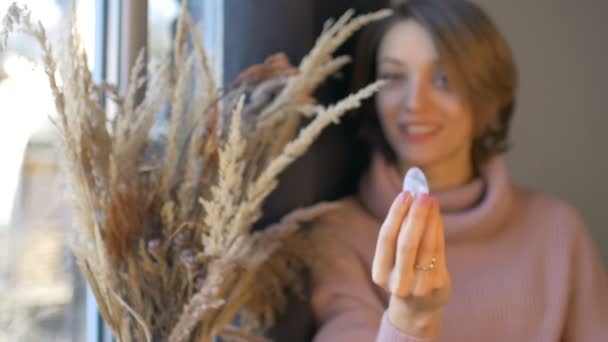 女人手里拿着用透明紫罗兰紫水晶制成的蛋黄蛋，站在窗边，旁边放着一盒小穗。女性健康概念、体形、植入或冥想 — 图库视频影像