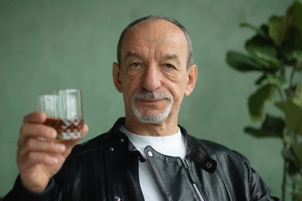 Крупный план зрелого мужчины, держащего стакан с виски возле лица и смотрящего в камеру, мужской портрет — стоковое фото
