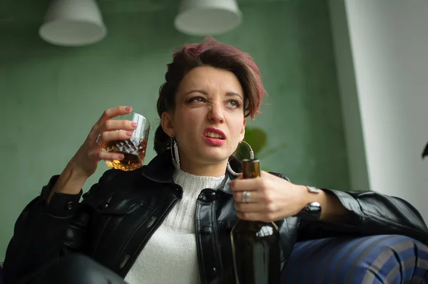 Young sad woman with dark pink hair with glam rock style look is drinking whisky from a glass with abomination grimace on the face, female alcoholism, alcohol addiction — Stock Photo, Image