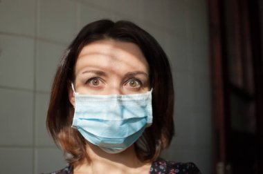 Coronavirus Covid-19 salgını. Pandemia sırasında yüzlerine cerrahi maske takmış genç bir kadının portresi. Üzüntü ve dehşetle kameraya bakıyor.