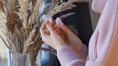 Pembe kuvarstan yapılmış iki yoni yumurtası ve vumfit için saydam menekşe ametisti tutan kadın eller pencerenin yanında dikenli vazo ile meditasyon yaparlar..