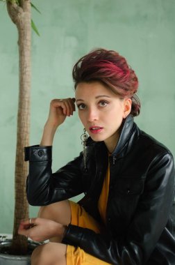 Glam rock tarzı koyu pembe saçlı, mohawk saçlı, sarı elbiseli, siyah deri ceketli, yakın plan kadın portresi olan güzel bir kız.