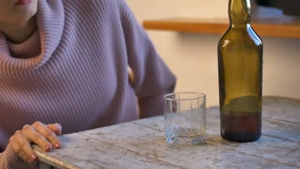 Sorglig kvinna i jeans och rosa tröja kommer hem, lägger dollar och nycklar på bordet och häller whisky på hennes glas från den gröna flaskan på grund av problemen, kvinnligt alkoholberoende — Stockvideo