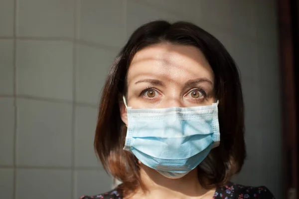 Brote de Coronavirus Covid-19. Retrato de una joven en aislamiento domiciliario con máscara quirúrgica en la cara para protegerse del virus durante la pandemia mirando a la cámara con tristeza y horror — Foto de Stock