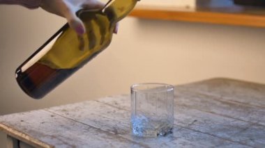 Kadın eli masadan yeşil bir şişe alır ve bardağa viski döker ve onu içer, alkol bağımlılığı konsepti.