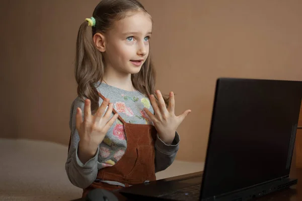 Маленькая ученица учится дома со своим учителем, используя видео-чат на черном ноутбуке из-за самоизоляции из-за пандемии Коронавируса Ковид-19. — стоковое фото