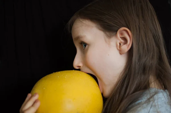 Widok z boku szalony zabawna dziewczynka próbuje ugryźć duży żółty pomelo w studio na czarnym tle, zdrowe jedzenie koncepcja — Zdjęcie stockowe
