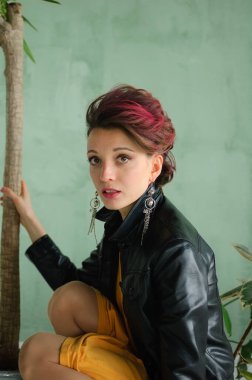 Glam rock tarzı koyu pembe saçlı, mohawk saçlı, sarı elbiseli, siyah deri ceketli, yakın plan kadın portresi olan güzel bir kız.