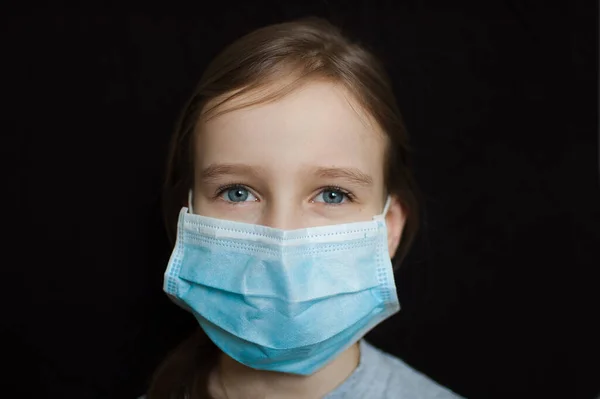 Brote de Coronavirus Covid-19. Niña rubia con máscara desechable azul claro para la protección del virus en el fondo negro en el estudio. Concepto de cuarentena —  Fotos de Stock