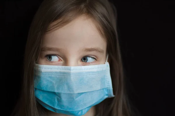 Retrato de estudio de una niña rubia sobre fondo negro con máscara desechable quirúrgica azul para la protección del Coronavirus Covid-19 durante el autoaislamiento mientras permanece en casa —  Fotos de Stock