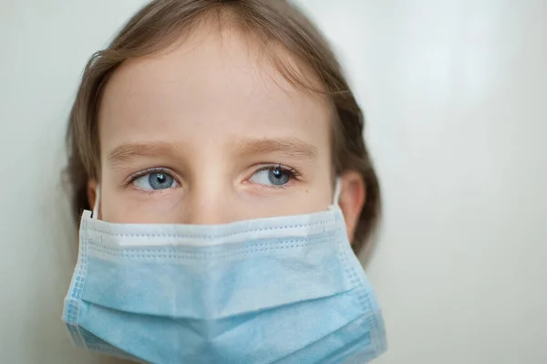 Un'epidemia di Coronavirus Covid-19. Piccola ragazza bionda con gli occhi azzurri che indossa una maschera usa e getta per la protezione del virus su sfondo bianco in studio. Concetto di dispositivo di protezione individuale — Foto Stock