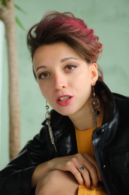 Glam rock tarzı koyu pembe saçlı, mohawk saçlı, sarı elbiseli, siyah deri ceketli, yakın plan kadın portresi olan güzel bir kız.