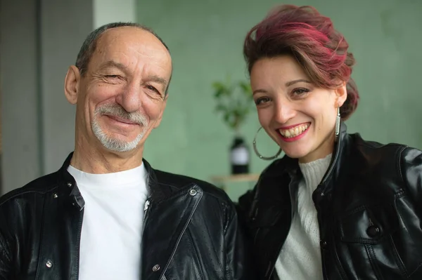 Retrato familiar emotivo de hija adulta y padre mayor en habitación tipo loft con plantas de interior. Gritando hombre y chica en chaquetas de cuero negro en estilo punk y mirando a la cara del otro —  Fotos de Stock