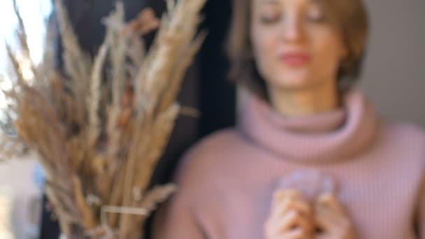 La chica muestra un masajeador de gua sha de masaje hecho de cuarzo rosa de piedra natural que se utiliza para estimular el sistema linfático y tiene un efecto anti edad, la cara femenina y las espiguillas no están en foco — Vídeos de Stock