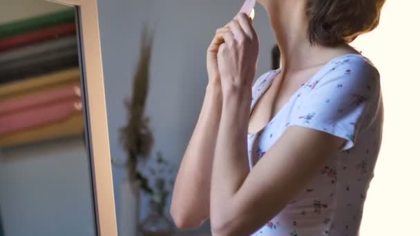 La ragazza fa un massaggio gua sha davanti allo specchio a casa utilizzando massaggiatore al quarzo rosa, pietra naturale. Sollevamento, stimolare il sistema linfatico e l'effetto anti età — Video Stock