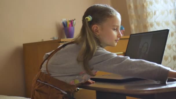 Kleines blondes Mädchen mit zwei Pferdeschwänzen lernt mit ihrem Lehrer per Videochat und schreibt etwas in Schulheft zu Hause wegen der Selbstisolierung durch Coronavirus Covid-19 — Stockvideo