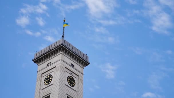 Stadhuis toren met een klok en de Oekraïense vlag in Lviv, West-Oekraïne, geïsoleerd op een blauwe hemel achtergrond — Stockvideo