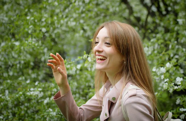 Sarışın, genç bir kadın bahar parkındaki çiçek açan büyük bir ağaçtaki birine merhaba diyor. Açık hava kadın portresi. — Stok fotoğraf