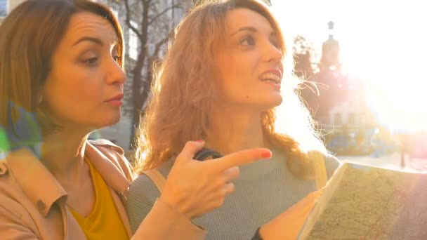 Happy young tourists holding a paper map of ancient European city early in the morning on empty square and pointing on some sightseeing place — Stock Video