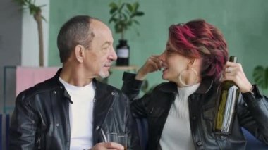 Koyu pembe saçlı, beyaz kazaklı ve siyah deri ceketli kızgın ve agresif bir kadının üst düzey babasıyla çatı katında içki içip çığlık attığı kapalı mekan videosu. Kadın alkolizmi