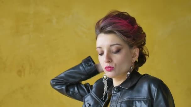 Glamorosa dama en estilo punk rock ropa de fiesta con pelo rosa oscuro en vestido casual, chaqueta de cuero negro, y pendientes largos está bailando sobre fondo amarillo — Vídeos de Stock