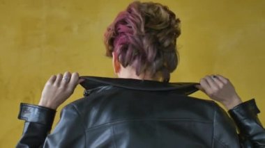 Punk rock tarzı parti kıyafetleri içinde göz kamaştırıcı bir kadın. Günlük kıyafetler içinde koyu pembe saçlar, siyah deri ceket ve sarı arka planda uzun küpeler.