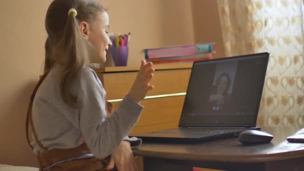 Little female pupil is studying at home with her teacher using video chat on her black laptop because of the self-isolation due to the pandemia of Coronavirus Covid-19 — Stock Video
