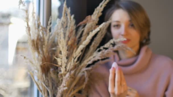 Ung kvinna visar yoni ägg gjorda av ros kvarts sten i handen står nära vas med spikelets inomhus. Koncept för kvinnors hälsa, vumfit, imitation eller meditation — Stockvideo