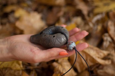 Turuncu manikürlü kadın eli sonbaharda ormanda seramik okarina tutar. Sakinleştirici sahne, geleneksel müzik kavramları