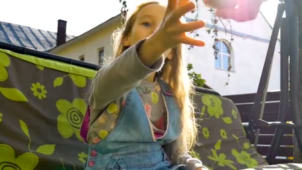 Niña rubia está comiendo manzana roja en un columpio al aire libre durante el día soleado de verano en el patio de recreo en el jardín, comida saludable, concepto de infancia feliz — Vídeo de stock