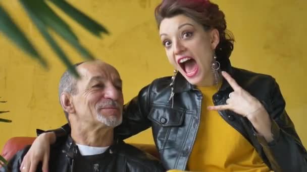 Yetişkin kız ve yaşlı babanın punk tarzı siyah deri ceketler giyip birbirlerine baktıkları duygusal aile portresi. Kız rock and roll jesti gösteriyor.. — Stok video