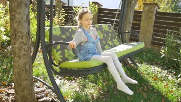 Lustiges lachendes Baby-Mädchen mit Spaß auf einer grünen Schaukelfahrt auf einem Spielplatz in einem sonnigen Sommergarten, glückliches Kindheitskonzept — Stockvideo