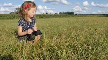 Sarışın kıvırcık kız, güneşli yaz gününde yeşil çimenlerde mavi kısa elbise ve koyu tozluklarla çekirge yakalar.