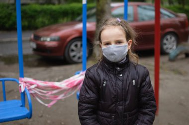 Kapalı oyun parkında gri maskeli ve koyu renk ceketli üzgün kızın portresi. COVID-19 'a karşı karantina önlemleri. Koronavirüs salgını.