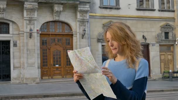 Frau verirrt sich in der alten europäischen Stadt, schaut auf eine Landkarte und sucht frühmorgens auf dem antiken Platz nach Orientierung. — Stockvideo