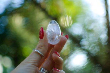 Vumfit, imbuilding veya meditasyon için şeffaf ametist kuvars yoni yumurta ile Kadın el. Gökyüzü ve gündoğumu arka plan açık havada ellerde parlayan kristal yumurta. Kadın sağlığı kavramı.