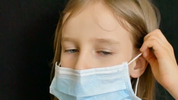 Coronavirus Covid-19 Ausbruch. Das kleine Mädchen blickt mit Glück in den Augen und Kaugummi im Mund in die Kamera. Positives Konzept während der Selbstisolation zu Hause in Schutzmaske — Stockvideo