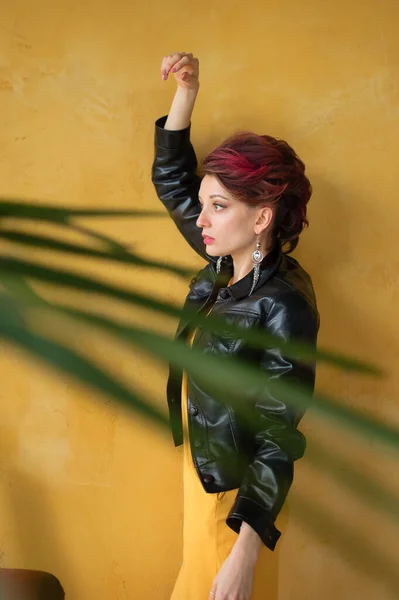 Seitenansicht der glamourösen Dame in Punk-Rock-Party-Kleidung mit dunkelrosa Haaren in lässigem Kleid, schwarzer Lederjacke und langen Ohrringen auf gelbem Hintergrund — Stockfoto