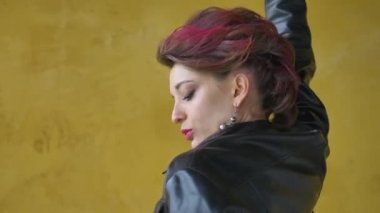 Punk rock tarzı parti kıyafetleri içinde göz kamaştırıcı bir kadın. Günlük kıyafetler içinde koyu pembe saçlar, siyah deri ceket ve sarı arka planda uzun küpeler.