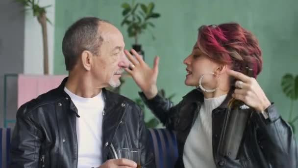 Vídeo interno de mulher bonita agressiva irritada com cabelo rosa escuro em camisola branca e jaqueta de couro preto bebendo com seu pai sênior no quarto de estilo loft e gritando. alcoolismo feminino — Vídeo de Stock