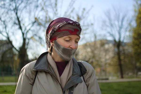 Mujer madura que usa mascarilla textil hecha a mano como accesorio y elemento protector durante el soleado día de primavera en el parque debido a la pandemia de coronavirus —  Fotos de Stock