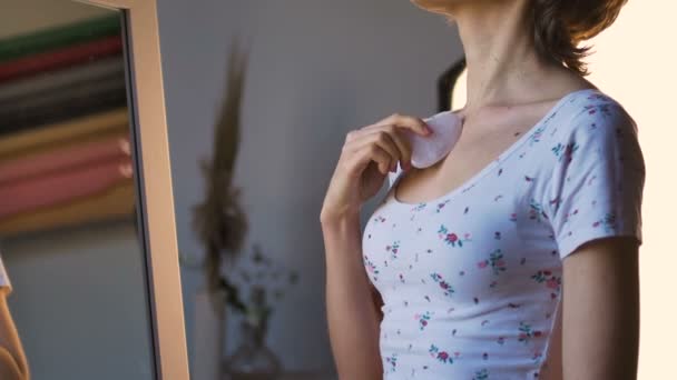 La ragazza fa un massaggio gua sha davanti allo specchio a casa utilizzando massaggiatore al quarzo rosa, pietra naturale. Sollevamento, stimolare il sistema linfatico e l'effetto anti età — Video Stock