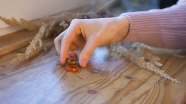 Kobiece dłonie z naturalnym manicure pokazują pomarańczowe i zielone kamienne pierścienie wykonane z agatu i opal perełek na drewnianym parapecie z kolcami na nim — Wideo stockowe