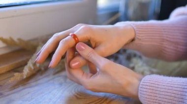 Doğal manikürlü kadın elleri, üzerinde çiviler olan tahta pencere pervazında turuncu ve yeşil değerli taşlardan yapılmış yüzükler gösteriyor.