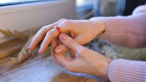 Female hands with natural manicure are showing orange and green gemstone rings made from agate and opal gems on wooden windowsill with spikelets on it — Stock Video