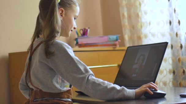 Achteraanzicht van een klein meisje met twee paardenstaarten die voor het scherm van haar zwarte laptop zitten en thuis studeren vanwege de zelfisolatie als gevolg van Coronavirus Covid-19. Afstandsonderwijs — Stockvideo