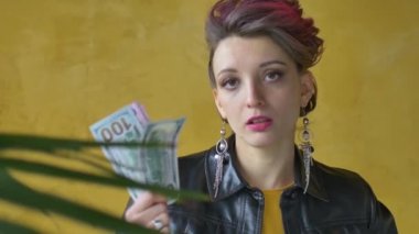 Punk rock tarzı parti kıyafetleri içinde parlak agresif bir bayan siyah deri ceketli koyu pembe saçlar ve sarı arka planda uzun küpeler para dolarları ve ellerinde Hryvnialar.
