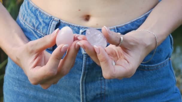 Vrouwelijke hand met een rozenkwarts en amethist kristallen yoni eieren. Womens gezondheid, eenheid met natuurbegrippen. Close portret van een onbekend meisje in jeans met een blote maag — Stockvideo